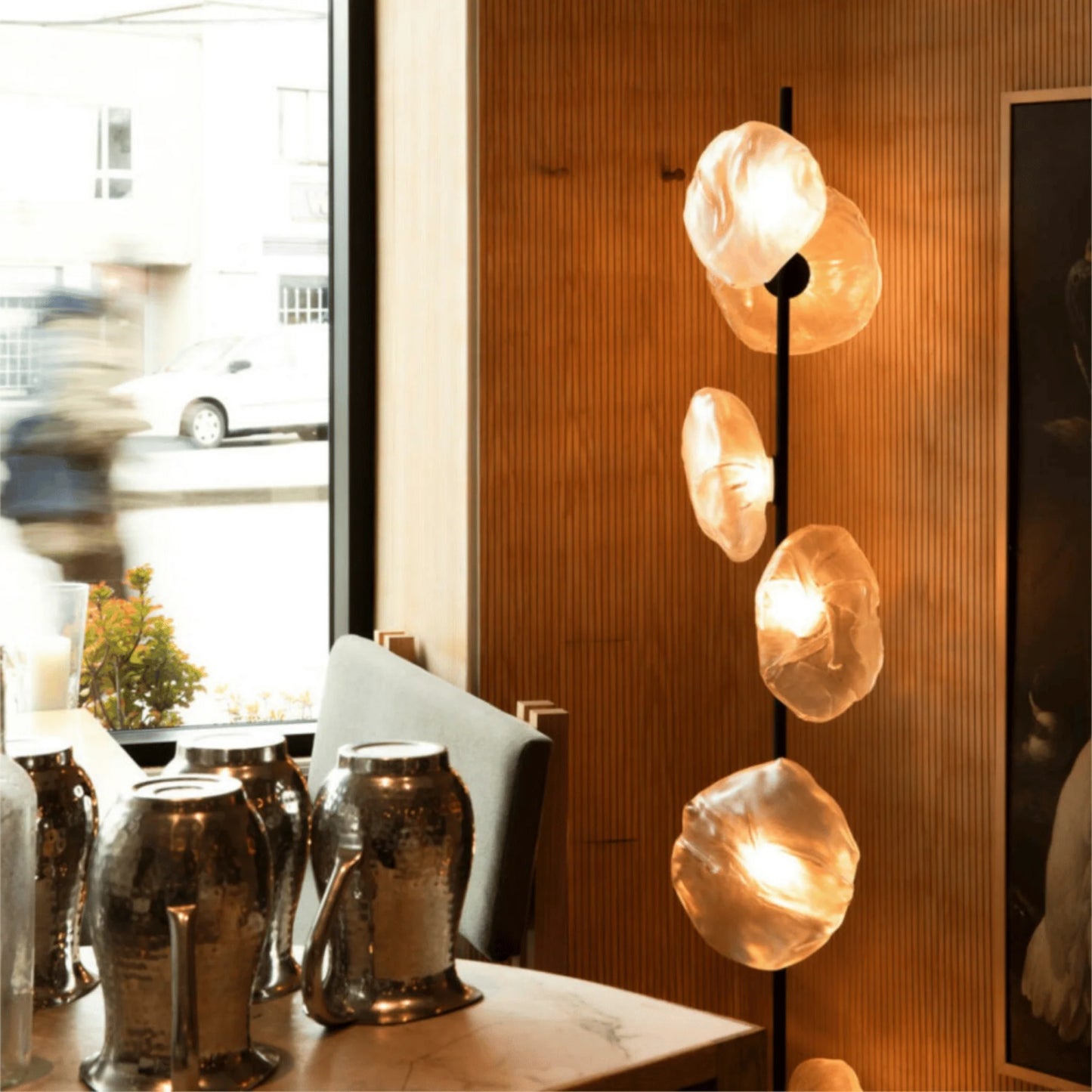 Modern glass LED floor lamp featuring organic, warm-glowing glass shades on a black stand, set in a stylish room with a wooden slatted wall.