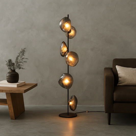 Modern glass LED floor lamp with a black stem and six glowing smoky grey organic glass shades, styled in a minimalist living room.