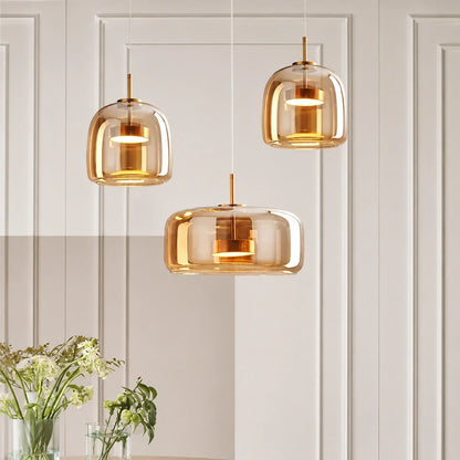 Three modern pendant lights with amber-tinted glass shades and gold accents hanging at different heights against a white panelled wall in a dining room.