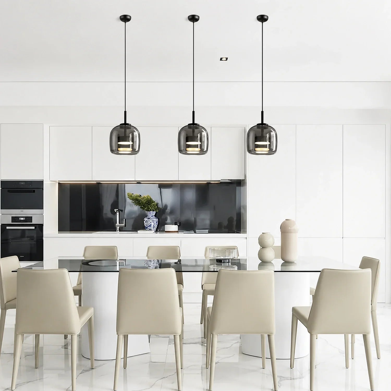 Three modern glass pendant lights with black fixtures hanging above a contemporary dining table in a bright, minimalist kitchen interior.