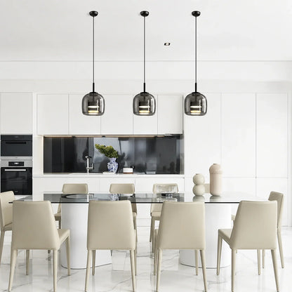 Three modern glass pendant lights with black fixtures hanging above a contemporary dining table in a bright, minimalist kitchen interior.