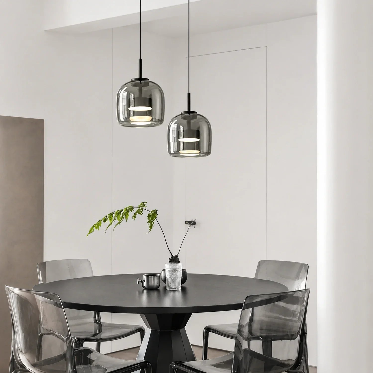 Two modern grey glass pendant lights with internal illumination hanging above a black circular dining table in a minimalist Nordic style interior.