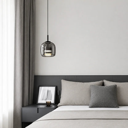 Modern glass pendant light with a smoked finish hanging above a minimalist bedside table in a contemporary bedroom with grey bedding and curtains.