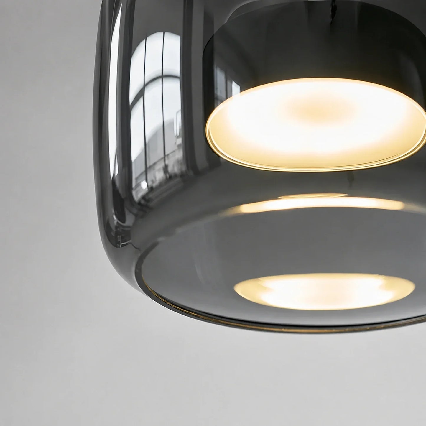 Close-up of a modern pendant light featuring a sleek, smoked glass shade with a warm, glowing internal light source against a neutral background.