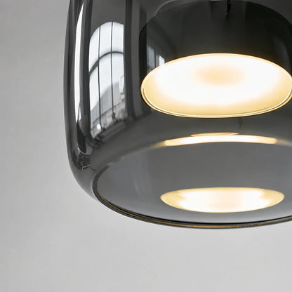 Close-up of a modern pendant light featuring a sleek, smoked glass shade with a warm, glowing internal light source against a neutral background.