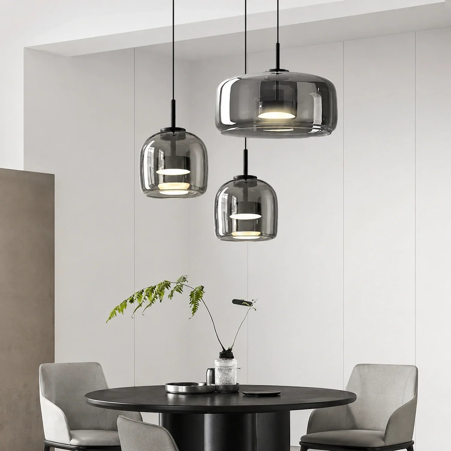 Three modern pendant lights with smoked glass shades hanging above a round black dining table in a contemporary Nordic style interior setting.