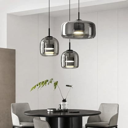Three modern pendant lights with smoked glass shades hanging above a round black dining table in a contemporary Nordic style interior setting.