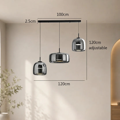 Modern linear triple-head pendant light with smoky grey glass shades in varying sizes, suspended from a black ceiling bar with adjustable drop height.