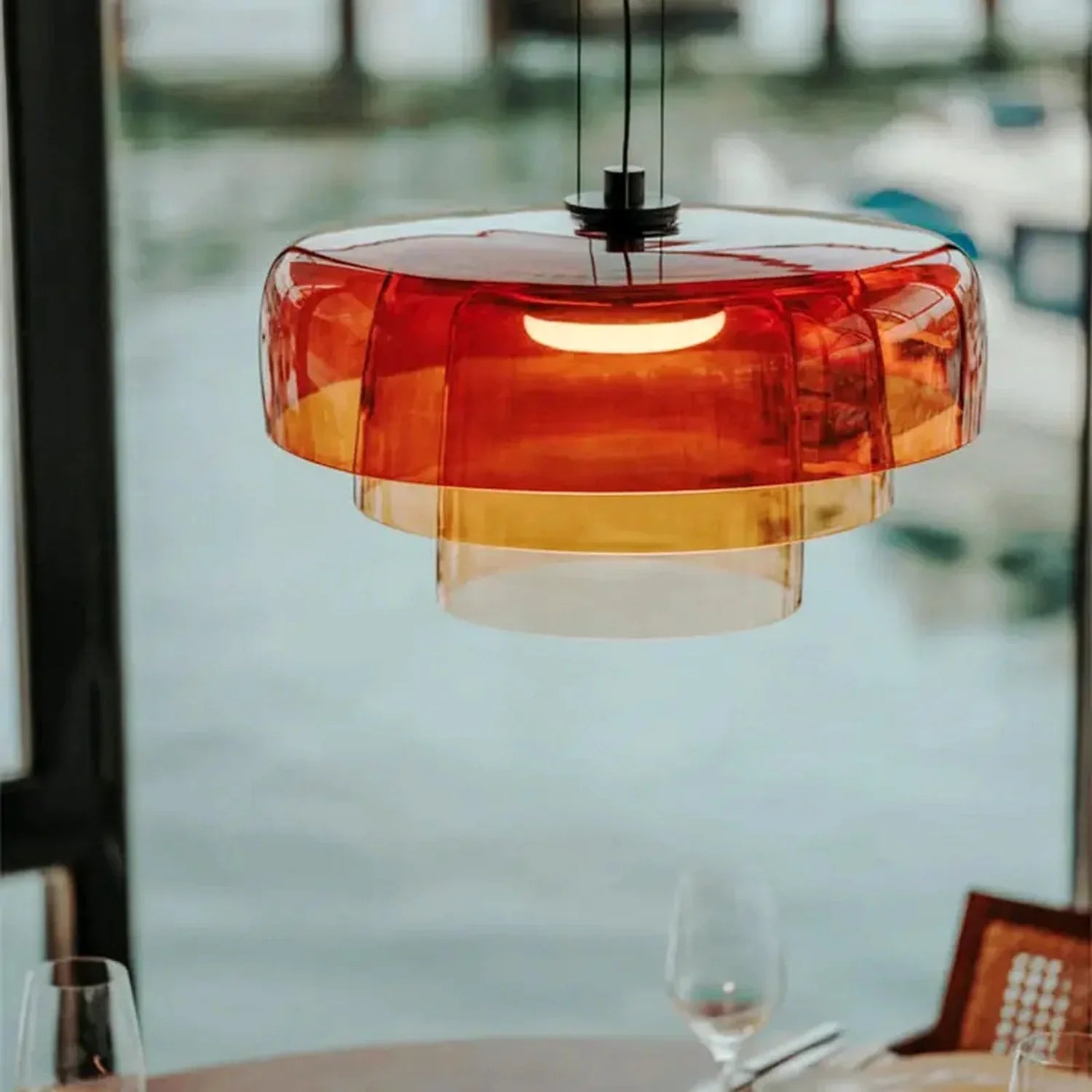 Modern tiered pendant light featuring translucent amber glass shades and an integrated LED, creating a warm glow above a dining room table setting.
