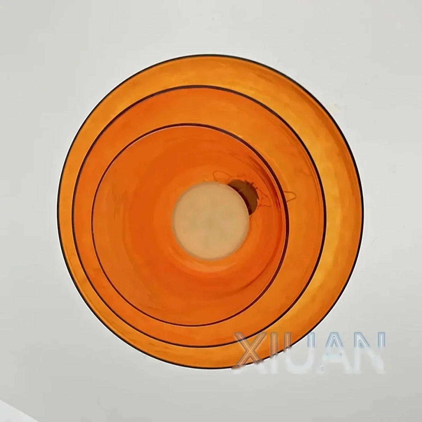 A direct upward view of a modern amber glass pendant light, showing the circular layered design and the central integrated LED light source.