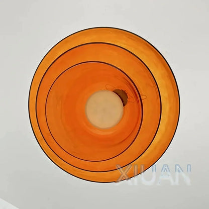 A direct upward view of a modern amber glass pendant light, showing the circular layered design and the central integrated LED light source.