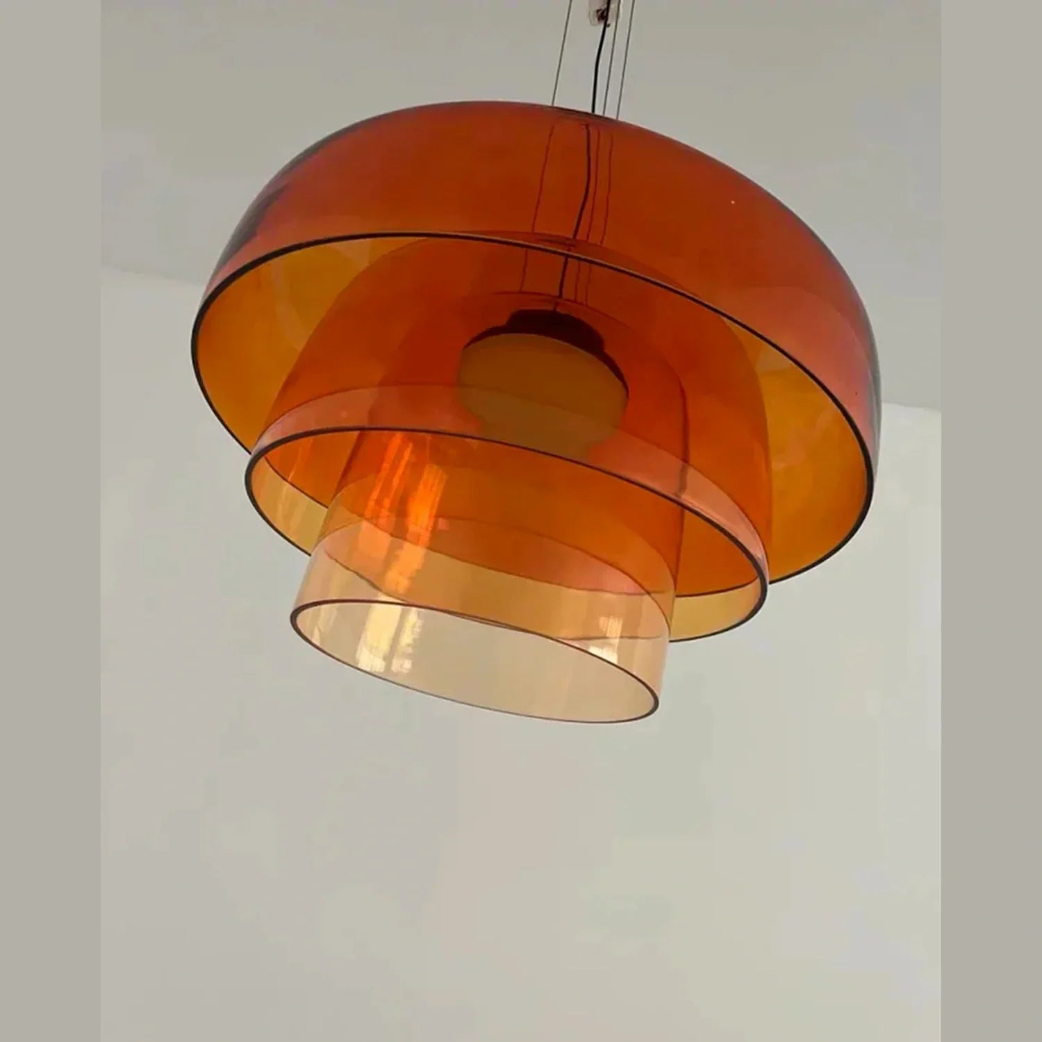 Modern pendant light featuring a tiered design with three concentric, translucent orange glass shades suspended against a plain white ceiling.