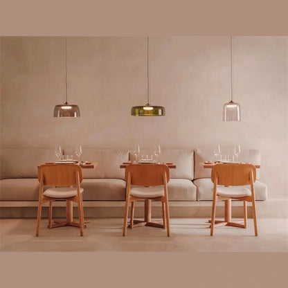 Three modern glass pendant lights with integrated LED illumination suspended above wooden dining tables and chairs in a minimalist dining room setting.