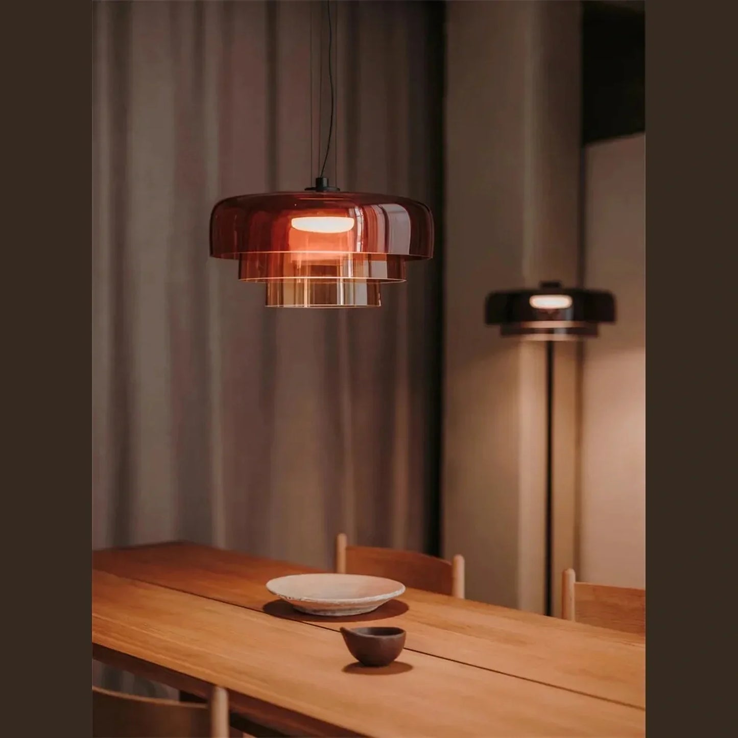 Modern tiered amber glass pendant light with integrated LED, suspended above a wooden dining table in a contemporary interior setting.