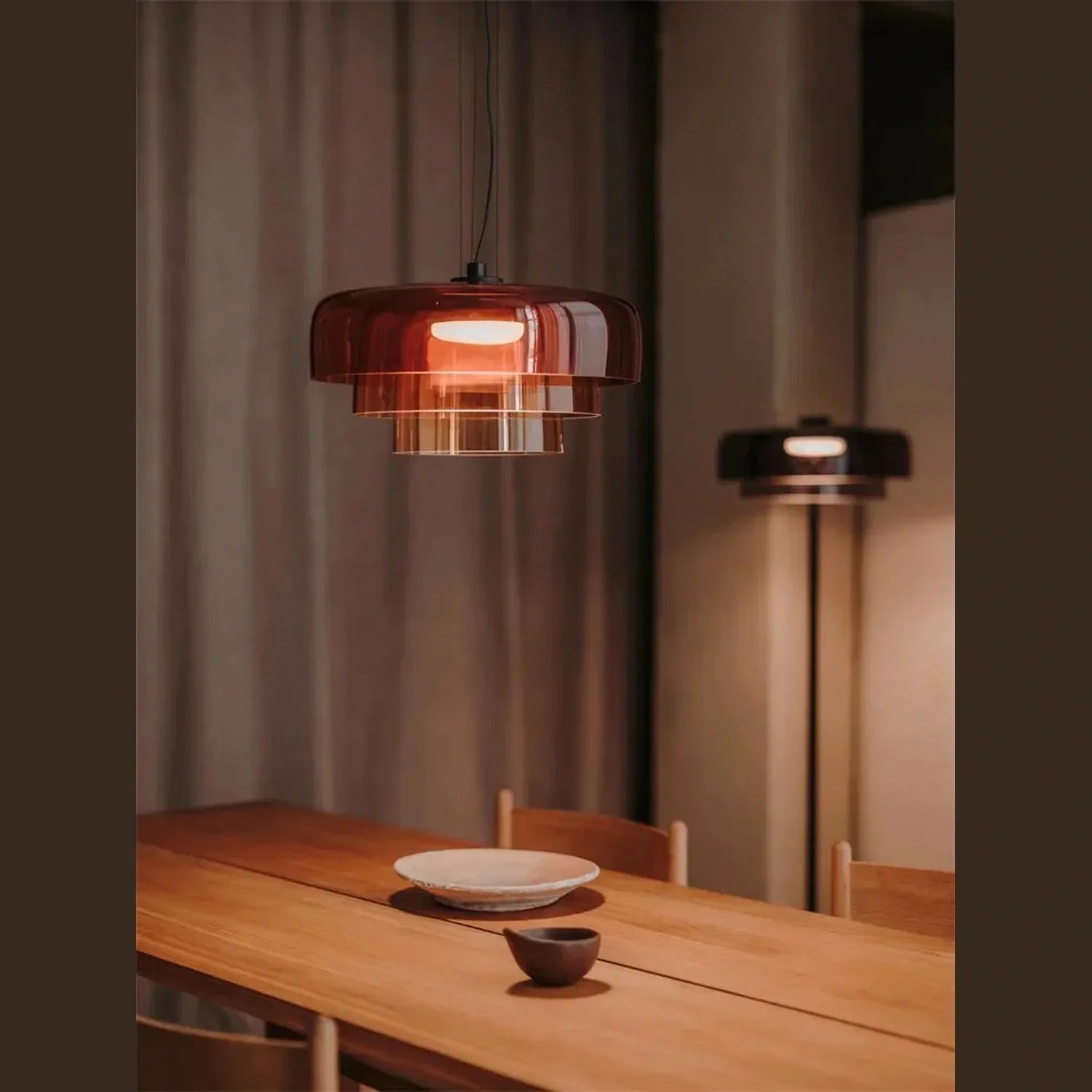 Modern tiered amber glass pendant light with integrated LED, suspended above a wooden dining table in a contemporary interior setting.