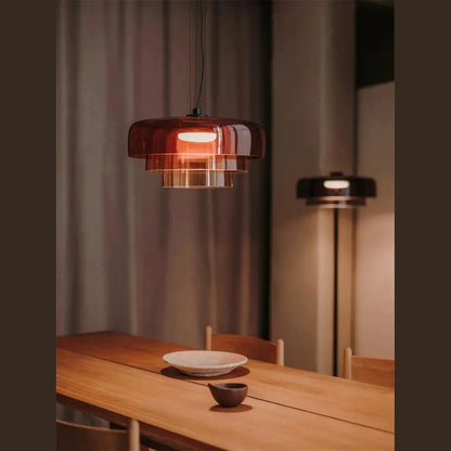 Modern tiered amber glass pendant light with integrated LED, suspended above a wooden dining table in a contemporary interior setting.