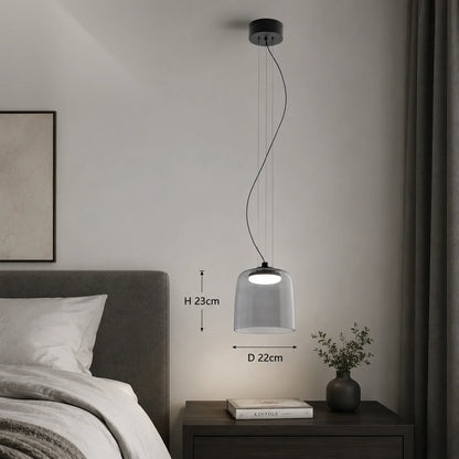 Modern grey glass pendant light with integrated LED suspended above a bedside table, showing 22cm diameter and 23cm height dimensions in a bedroom.