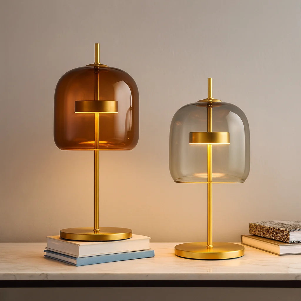Two modern table lamps with gold metal bases and amber and grey glass dome shades, displayed on a marble surface with stacked books.
