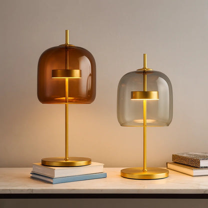 Two modern table lamps with gold metal bases and amber and grey glass dome shades, displayed on a marble surface with stacked books.