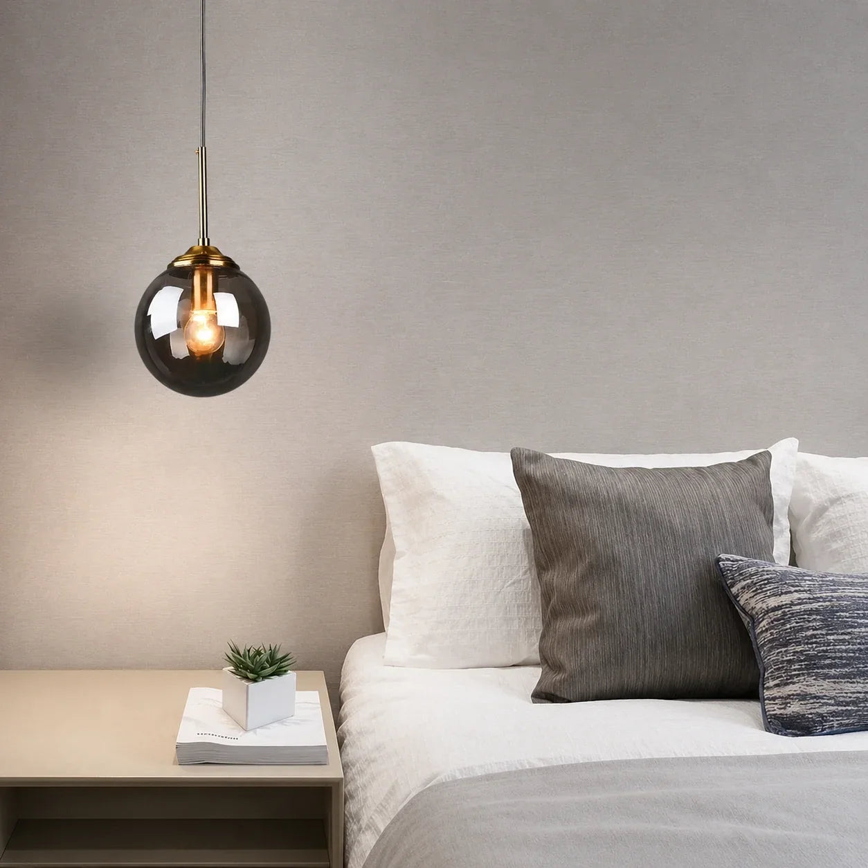 Modern globe glass pendant light with a brass fitting hanging above a bedside table in a contemporary bedroom setting with neutral decor.