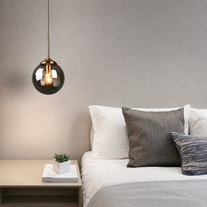 Modern globe glass pendant light with a brass fitting hanging above a bedside table in a contemporary bedroom setting with neutral decor.