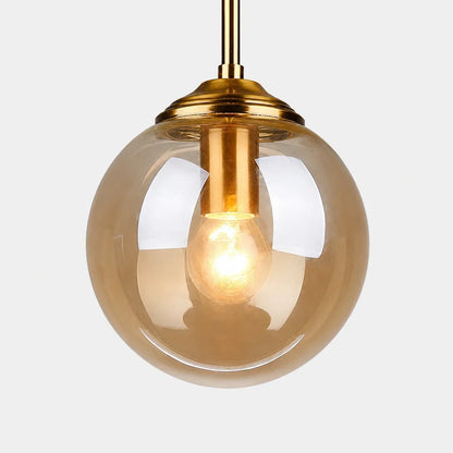 Modern globe pendant light featuring a warm tinted glass shade and a polished brass fitting, perfect for stylish bedroom or kitchen interior lighting.
