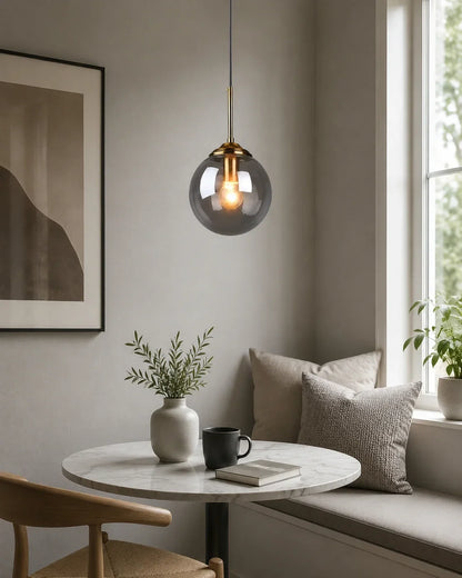 Modern globe pendant light with a smoked glass shade and brass fitting, hanging above a marble bistro table in a stylish, neutral-toned dining nook.