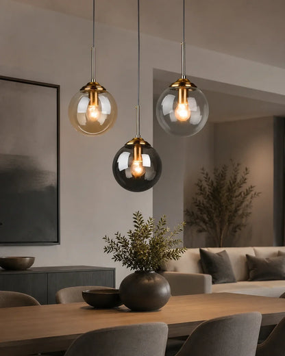 Three modern globe glass pendant lights with brass fittings hanging above a dining table in a contemporary living space with warm interior lighting.