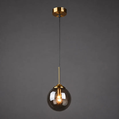 Modern globe glass pendant light featuring a smoky grey glass shade, brass fixture, and a glowing warm white bulb against a dark background.
