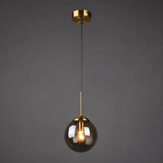 Modern globe glass pendant light featuring a smoky grey glass shade, brass fixture, and a glowing warm white bulb against a dark background.