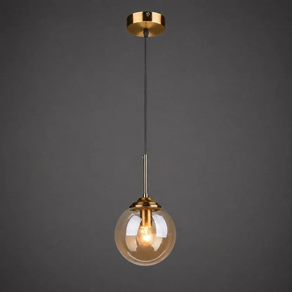 Modern globe pendant light featuring an amber glass shade and brushed brass finish, suspended by a black cable against a dark grey background.