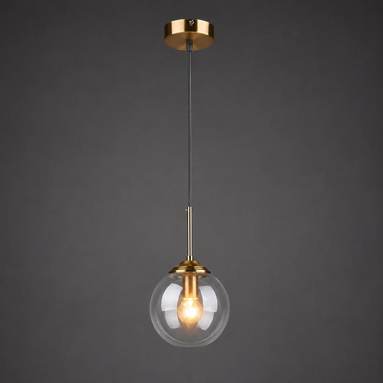 Modern globe pendant light with a transparent glass shade and brass finish ceiling rose, perfect for stylish bedroom or kitchen interior lighting.