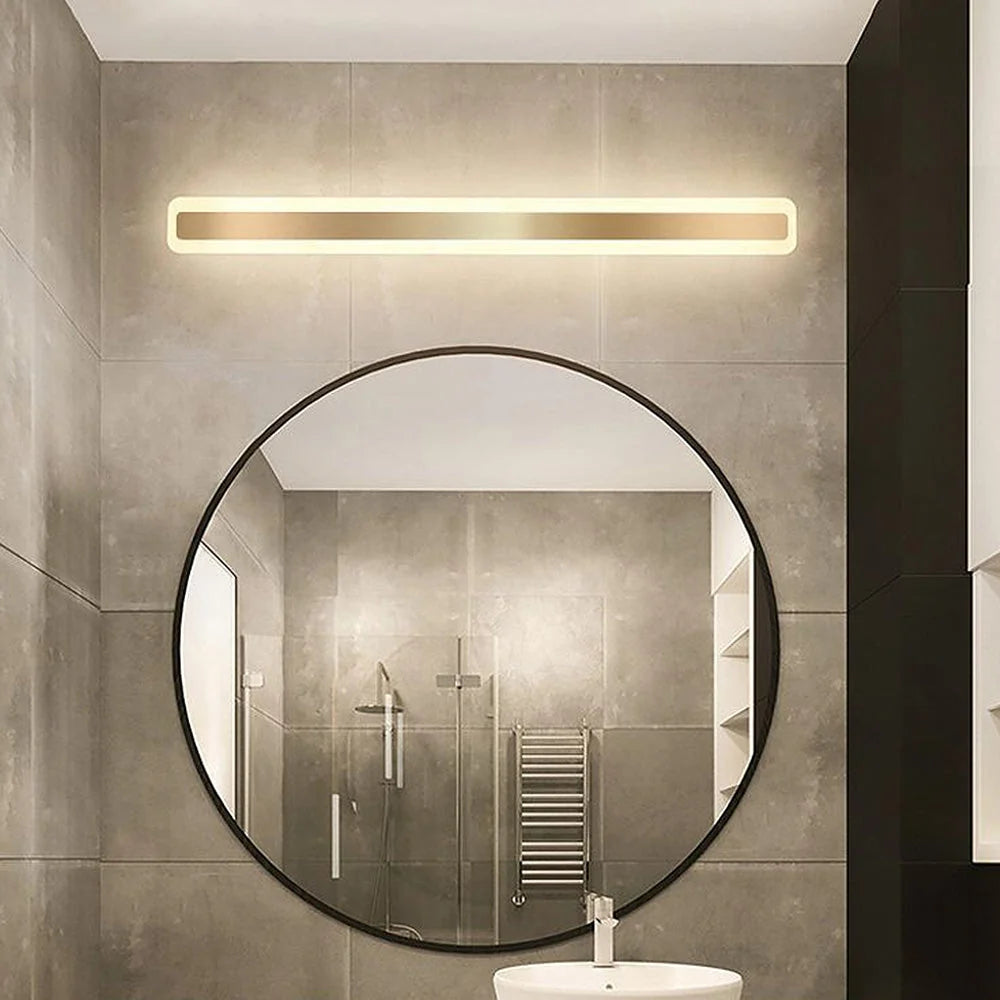 Modern linear LED bathroom wall light with a gold finish mounted above a large circular mirror in a contemporary tiled bathroom setting.