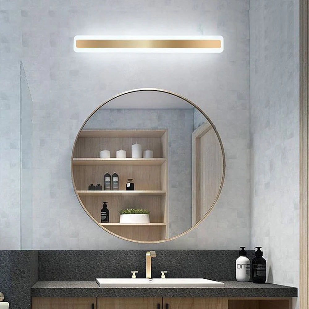 Modern linear LED bathroom wall light with a gold finish mounted above a circular mirror in a contemporary bathroom vanity setting with white light.