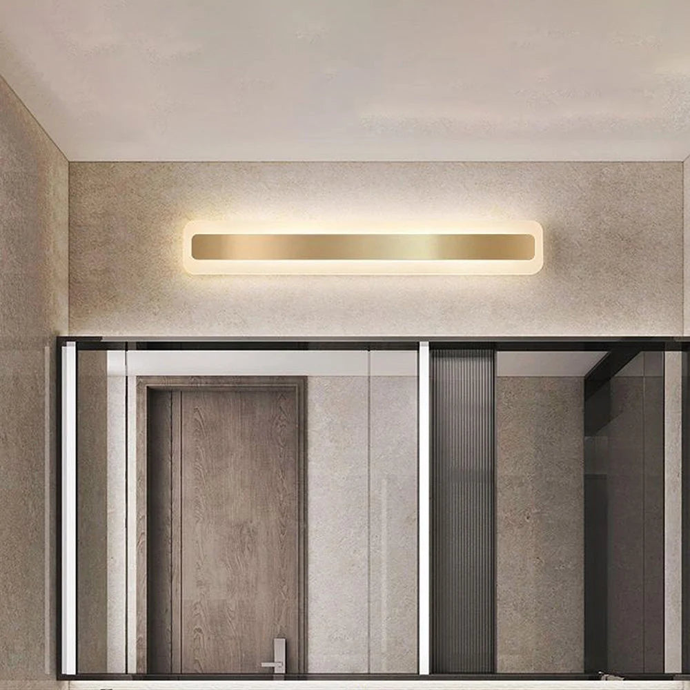 Modern linear LED bathroom wall light with a sleek gold finish mounted above a vanity mirror, providing warm ambient illumination in a contemporary room.