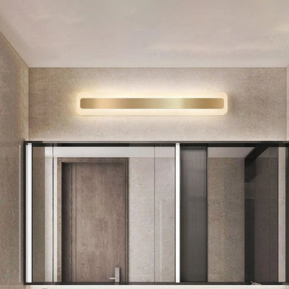 Modern linear LED bathroom wall light with a sleek gold finish mounted above a vanity mirror, providing warm ambient illumination in a contemporary room.