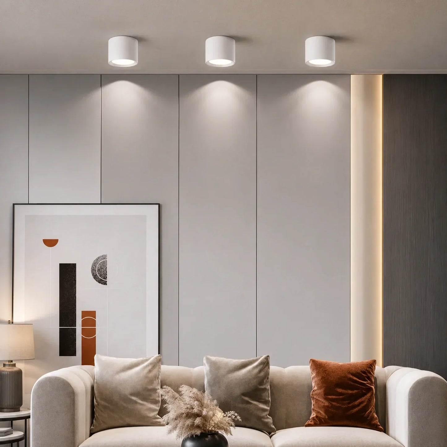 Three white surface-mounted modern LED ceiling lights casting light down a grey panelled wall above a sofa in a contemporary living room.