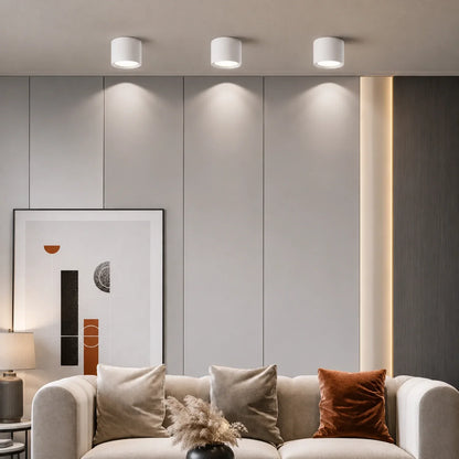 Three white surface-mounted modern LED ceiling lights casting light down a grey panelled wall above a sofa in a contemporary living room.