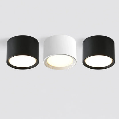 Three minimalist surface-mounted LED ceiling downlights in black and white, featuring a sleek cylindrical aluminium design with warm glowing light.