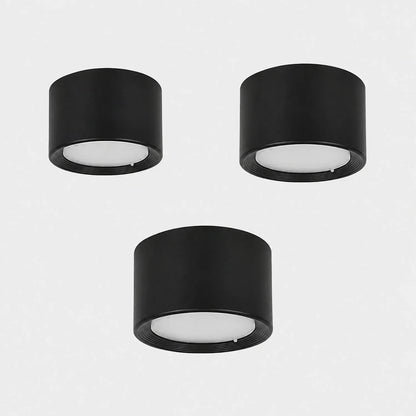 Three minimalist black cylindrical surface-mounted LED ceiling downlights with white diffusers, arranged on a plain light grey background.