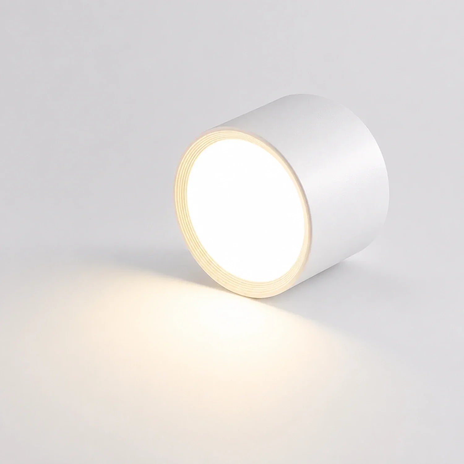 Modern white cylindrical LED ceiling light casting a warm white glow. This surface-mounted aluminium downlight features a minimalist design.