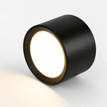 Minimalist black aluminium surface-mounted LED downlight, illuminated with a warm white glow, shown on a plain white background.