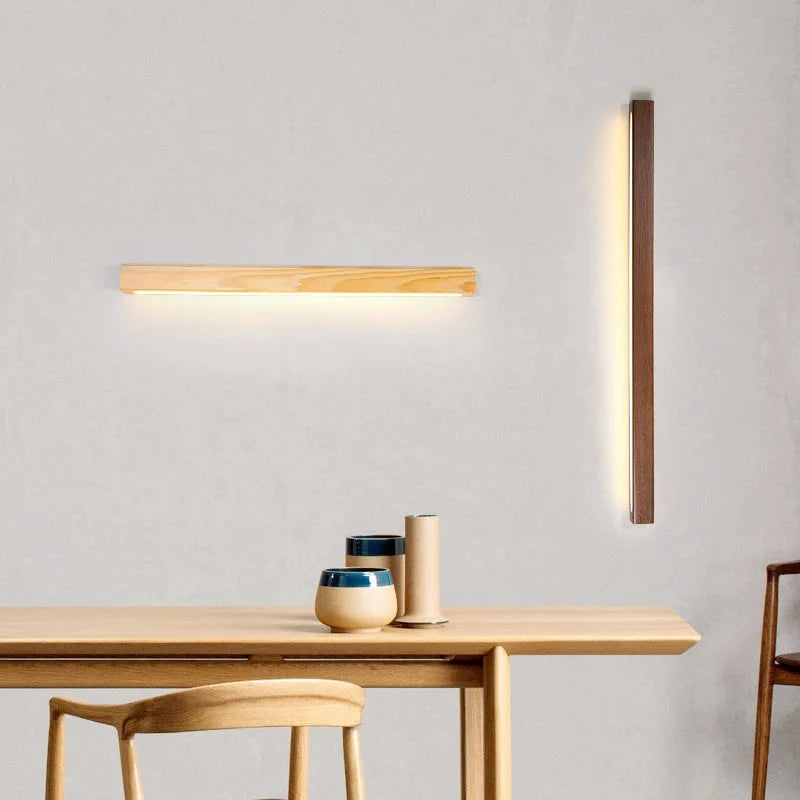Modern LED dimmable wood wall lights in light and dark wood finishes, mounted horizontally and vertically on a grey wall above a dining table.