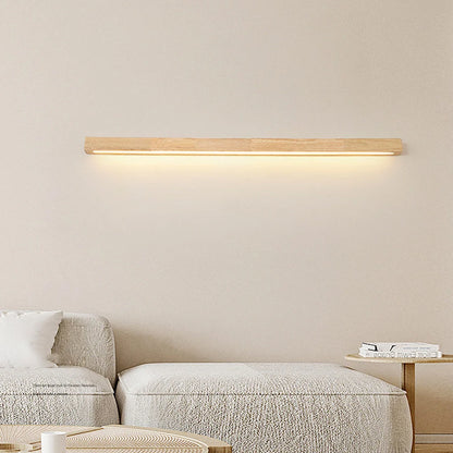 A modern LED dimmable wood wall light emitting a warm downlight glow on a neutral wall, mounted above a contemporary light-coloured fabric sofa.