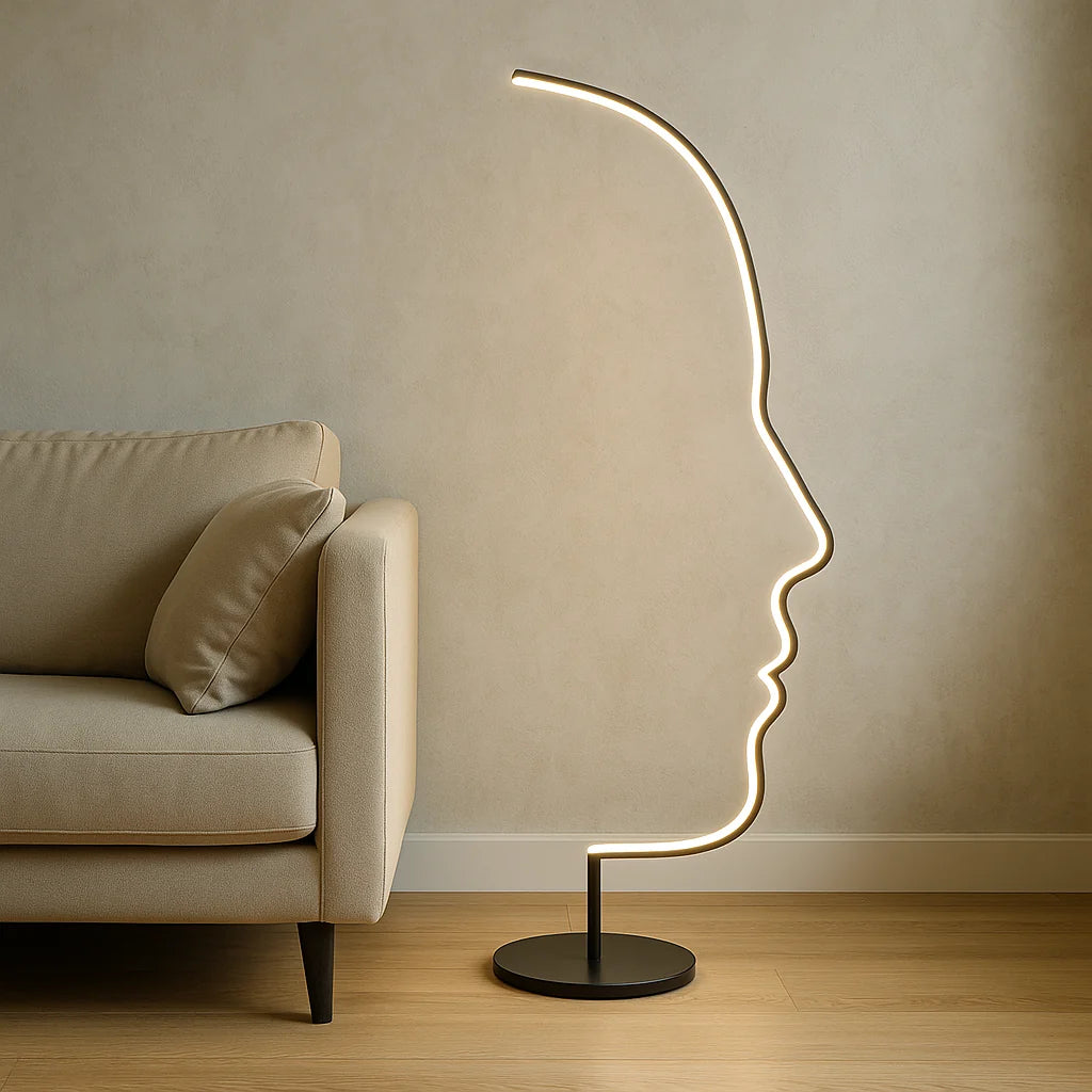 A modern LED floor lamp with an artistic human face profile design, glowing with warm light next to a beige sofa in a contemporary living room.