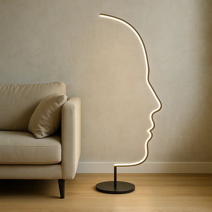A modern LED floor lamp with an artistic human face profile design, glowing with warm light next to a beige sofa in a contemporary living room.