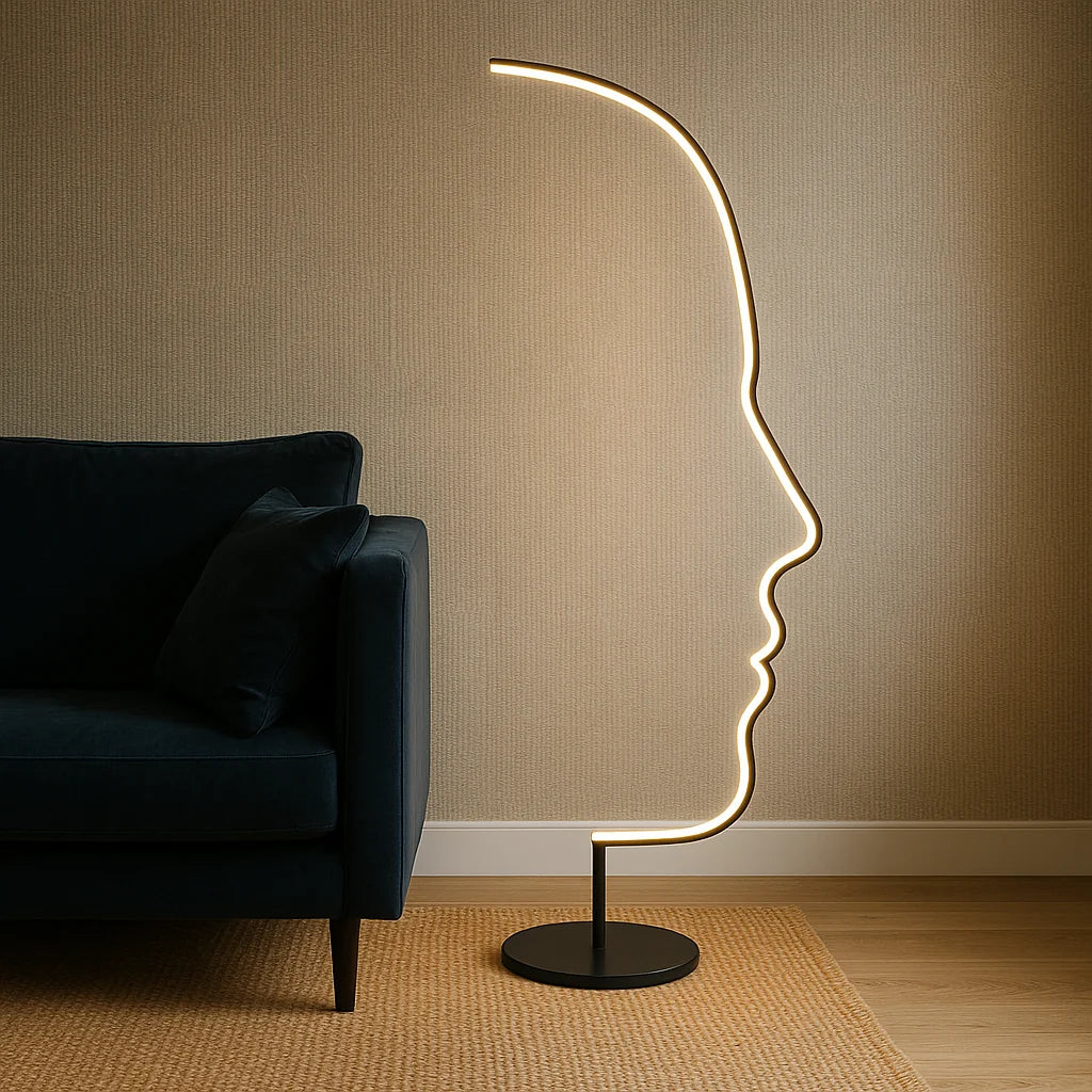 Modern LED floor lamp with an artistic human face profile design, glowing with warm light next to a dark blue sofa in a cosy living room.