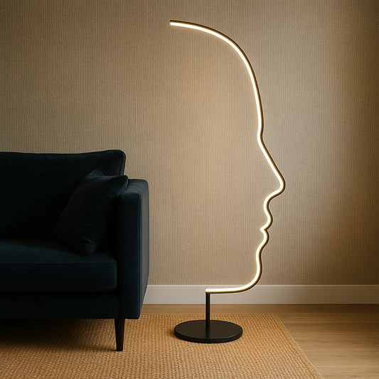 Modern LED floor lamp with an artistic human face profile design, glowing with warm light next to a dark blue sofa in a cosy living room.