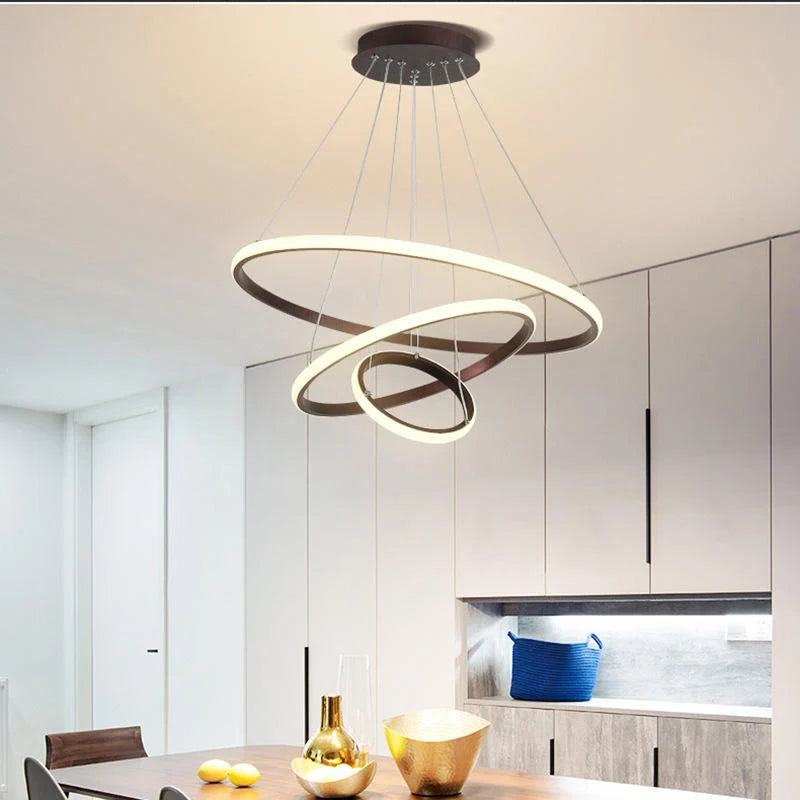 Modern three-ring LED ceiling light suspended above a dining table in a contemporary kitchen, featuring a sleek design with warm, dimmable illumination.