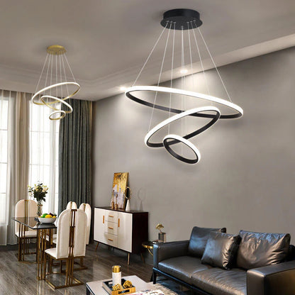 Modern three-ring LED ceiling lights in black and gold finishes suspended above a contemporary dining and living room area with elegant furniture.